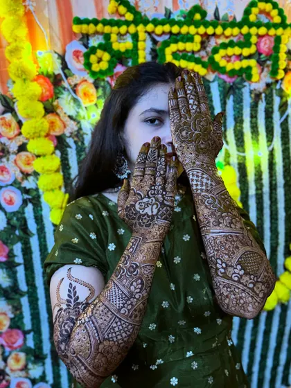 A playful peek-a-boo pose from a happy bride, showing off her intricate traditional henna with an elephant detail.