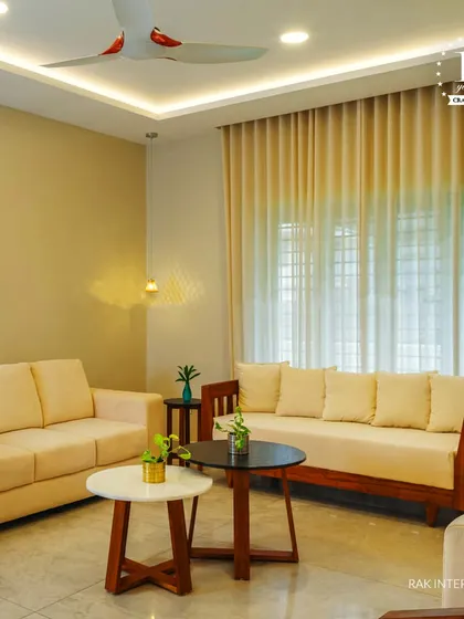A simple and warm living room with comfortable beige sofas and wooden frames. The nested coffee tables and indoor plants add a touch of modern, minimalist charm.