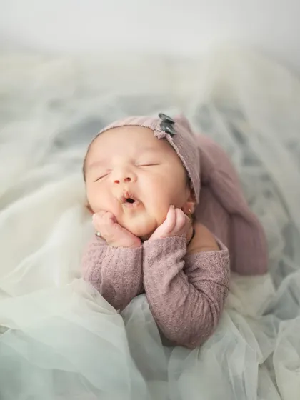 Another adorable sleepy expression, with chubby cheeks squished between tiny hands. This classic newborn pose is a favorite among parents.