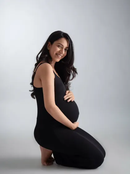 A simple and elegant kneeling portrait in a classic black dress. The clean grey background puts all the focus on the mother-to-be's happy expression and beautiful bump.