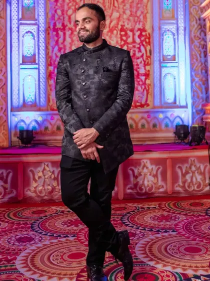 A classic Jodhpuri, or bandhgala, suit in a dark, self-patterned fabric. Paired with tailored trousers, this is a timeless and formal option for any wedding event.