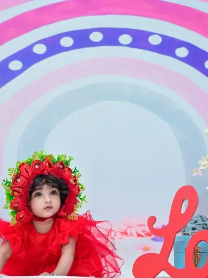 A wide shot of the rainbow-themed setup, showing the baby girl in her red dress amidst the colorful props and flowers.