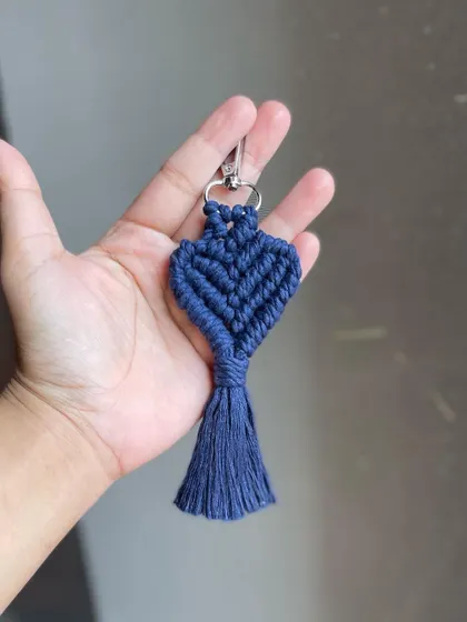Holding the navy blue heart keychain. The macrame knots create a beautiful, sturdy texture.