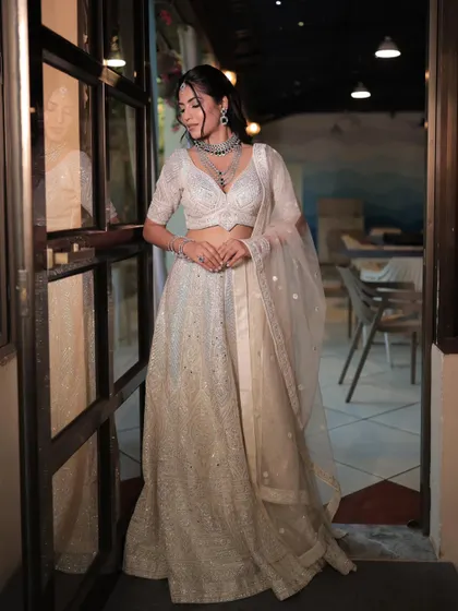 A candid shot of a model in a white lehenga, showing the full outfit in a relaxed setting. The simple diamond jewellery adds a touch of sparkle.