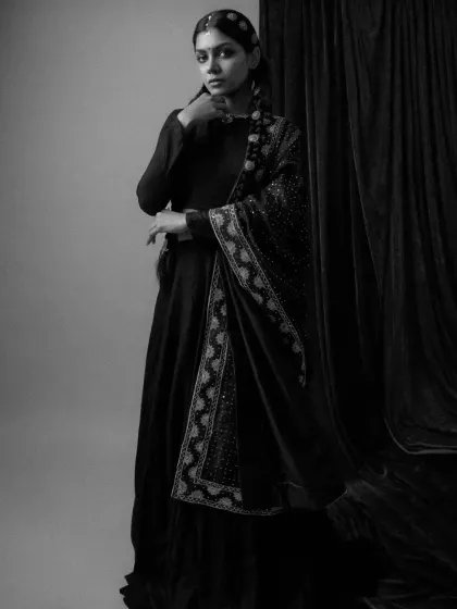A full-length black and white portrait from 'Amodini'. The styling showcases the flow of the embroidered dupatta against the dark anarkali, creating a dramatic and graceful silhouette.