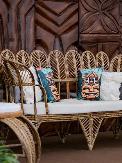 A stylish seating nook with a cane sofa and themed cushions. The intricate carving of the wooden backdrop adds a rich layer of texture and artistry to the space.