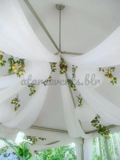 The ceiling decor for a Sicilian-themed party. White fabric is elegantly draped across the ceiling, interspersed with hanging paper lanterns and branches of fresh lemons, creating a light and airy feel.