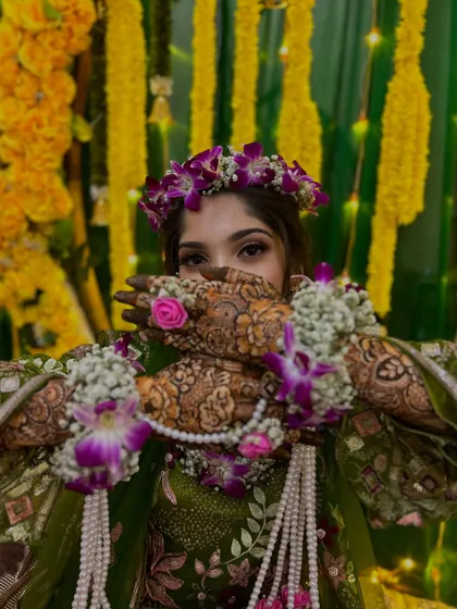 A beautiful bride peeking through her hands, adorned with floral jewelry that matches her henna.
