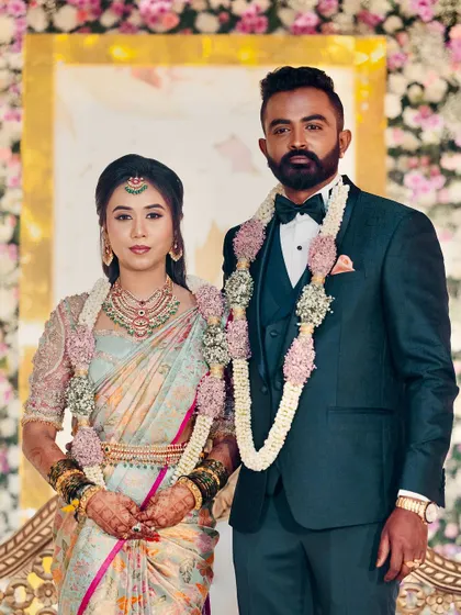 A formal portrait of the reception couple. The groom's dark tuxedo and bow tie are a timeless choice, looking sharp next to the bride's pastel blue and pink saree.