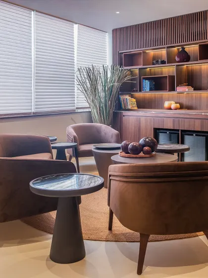 A cozy lounge corner at the ZOII wellness club, featuring custom-designed armchairs in a warm brown fabric. The fluted walnut wall paneling and soft lighting create an inviting space for pause and reflection.