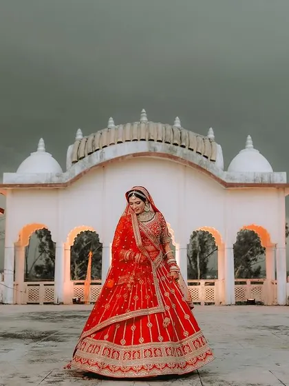 A full-length portrait of the bride in her red lehenga, showcasing the grandeur of her attire against the beautiful architecture.