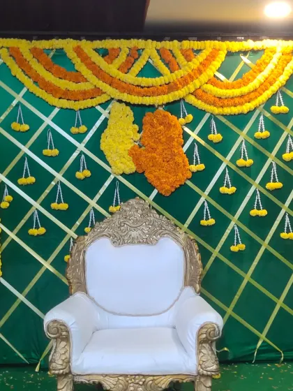 A traditional decor piece for a ceremony, featuring a green backdrop with yellow marigold garlands.