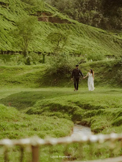 The couple walks through a picturesque valley with tea plantations in the background, a perfect example of a destination pre-wedding shoot in Kerala.