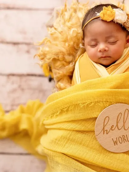 "Hello World!" This little one is perfectly swaddled in a yellow wrap, announcing her arrival in style. The wooden sign adds a lovely personal touch.
