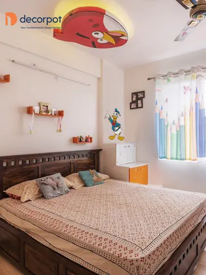 A fun kids' bedroom featuring an Angry Bird-themed false ceiling light. The room also includes a traditional wooden bed and a compact, wall-mounted study table.