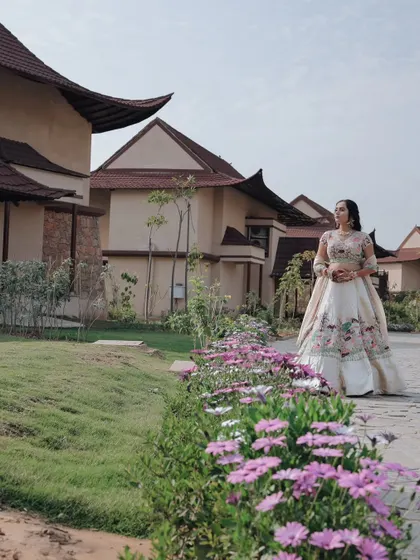 A wide shot of the bride in her floral lehenga, standing in a beautifully landscaped garden at the resort venue.