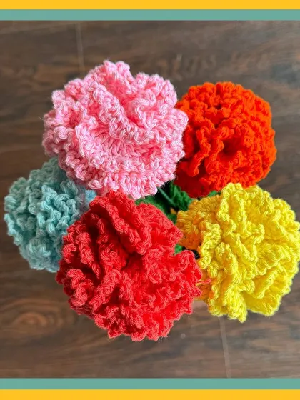 A top-down view of a colorful bunch of crochet carnations. I make these in a variety of colors like pink, red, yellow, orange, and light blue, each with fluffy, textured petals that look just like the real thing.