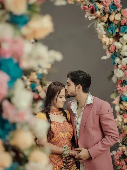 A romantic close-up of the couple framed by a colorful floral arch. The groom's gentle kiss on the bride's forehead is a classic, tender moment.