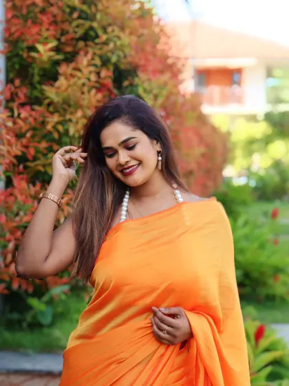 A client looking beautiful in a simple and elegant orange satin saree, perfect for a daytime event.