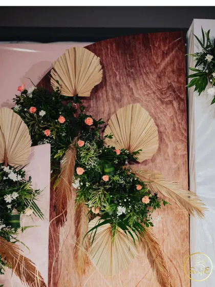A close-up of a modern floral arrangement using dried palm leaves and soft-colored roses.