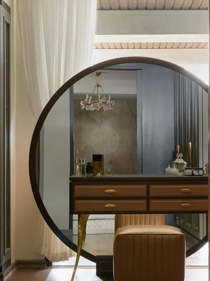 A close-up of the vanity in the master suite, featuring a large round mirror and a delicate floral chandelier reflected in it. The design combines classic elegance with modern forms.