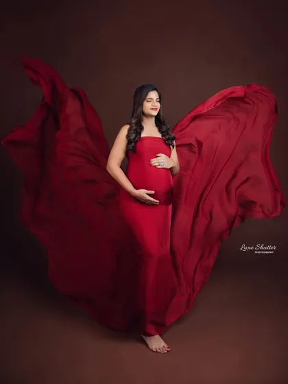 A serene moment, with the mother-to-be cradling her bump. The flowing red fabric seems to embrace her, symbolizing the love that surrounds her.