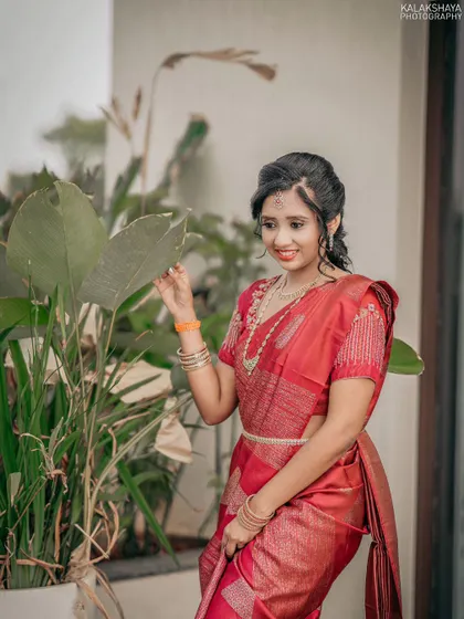 A lovely portrait of a bride in a red saree, posing naturally among plants.