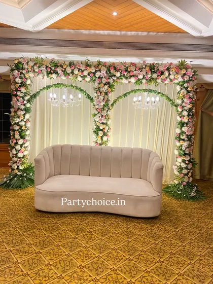 Our engagement stages are designed for elegance and romance. This setup features two graceful floral arches over a modern sofa, set against a clean, draped backdrop with soft lighting, creating a perfect photo opportunity for the couple.