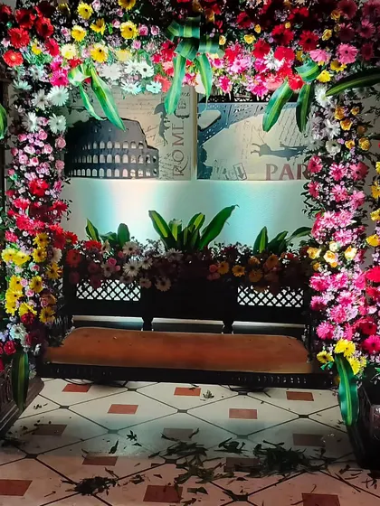 A floral swing setup perfect for taking pictures during a home event. The swing is framed by a dense arch of multi-colored flowers, creating a beautiful and festive photo opportunity for guests.