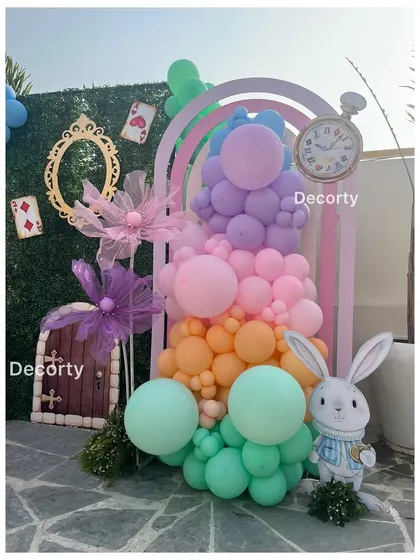 A whimsical photo spot with a rainbow-colored balloon arrangement, a plush white rabbit, and a small door prop.