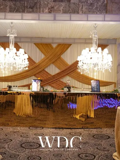 A luxurious bar setup with a reflective golden front, elegant chandeliers, and a backdrop of crisscrossing drapes, perfect for a grand celebration.