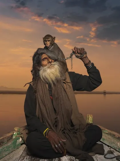 Monkey Baba and his companion on a boat during a beautiful sunset over the Ganga. The warm light adds a sense of peace and finality to their timeless story.