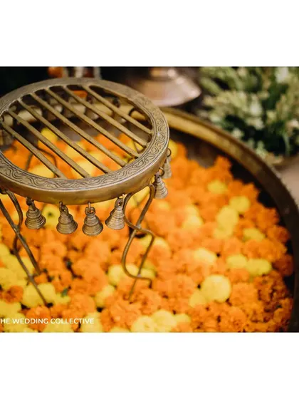 An antique brass stand with tiny bells, placed in a bowl of fresh marigolds. This small vignette from a Haldi ceremony showcases our love for combining traditional artifacts with fresh, vibrant florals to create beautiful textures.