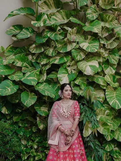 A beautiful portrait using nature as a backdrop. The bride stands against a wall of lush, green leaves, which makes her pink lehenga pop, creating a fresh and vibrant look.