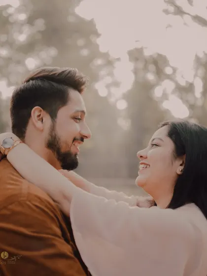 A beautiful, soft-focus shot of a couple smiling at each other. The warm, hazy light creates a dreamy and romantic atmosphere, perfect for a pre-wedding close-up.