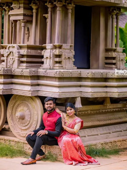 A classic portrait of a couple by a stone chariot. The bride's red and gold saree and the groom's black and red outfit create a striking combination.