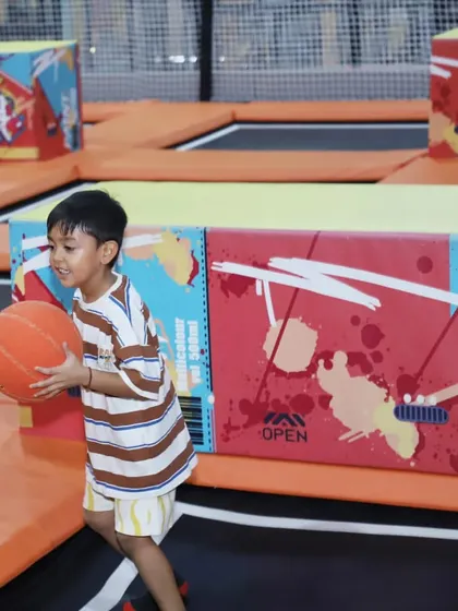 A boy gets ready to shoot a basket while bouncing, a fun challenge for older kids in our trampoline arena.