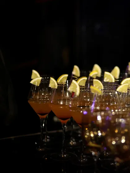 A row of elegant glasses filled with a golden-hued mocktail, each garnished with a fresh lemon slice. This image captures the simple elegance and readiness of our beverage service.