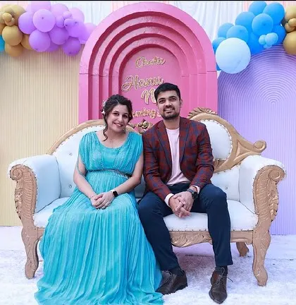 The happy parents-to-be posing at their baby shower. The backdrop features pastel-colored arches and a beautiful balloon arrangement.