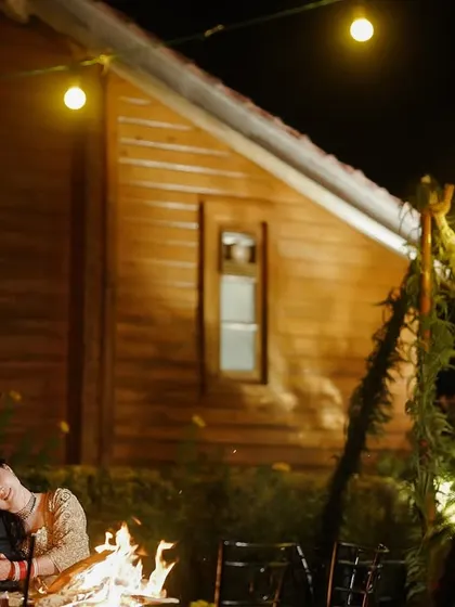 A cozy, romantic shot of a couple by a bonfire at night. The string lights and warm fire create an intimate and magical atmosphere.