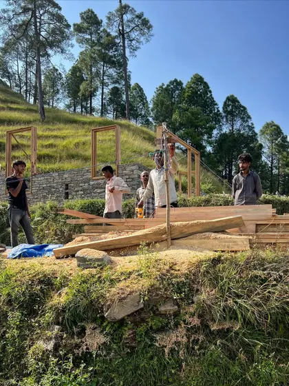 The process of building in the mountains is a partnership with the land and its people. Here, timber frames are being set by local artisans against the backdrop of the Himalayan foothills, a testament to handmade architecture.