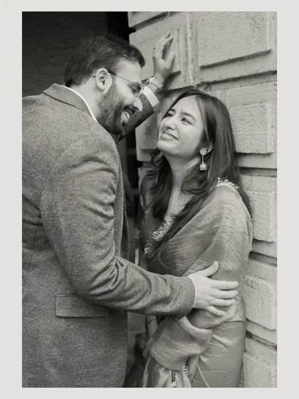 A close, intimate moment shared against a textured wall. The black and white edit emphasizes their expressions and the genuine affection between them.