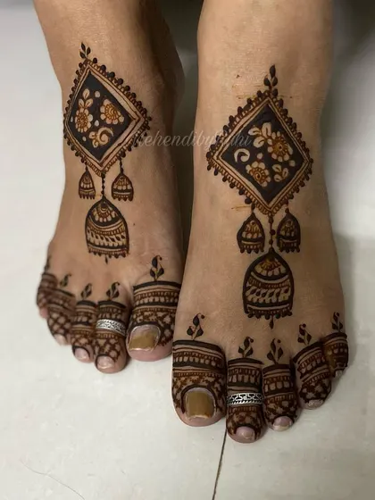 A unique and modern foot design featuring a geometric diamond shape with hanging 'jhumka' or earring motifs.