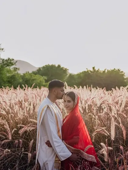 A romantic portrait of a couple in a field of pampas grass, with the hills of Rajasthan in the background. The soft, golden light creates a dreamy and ethereal mood.