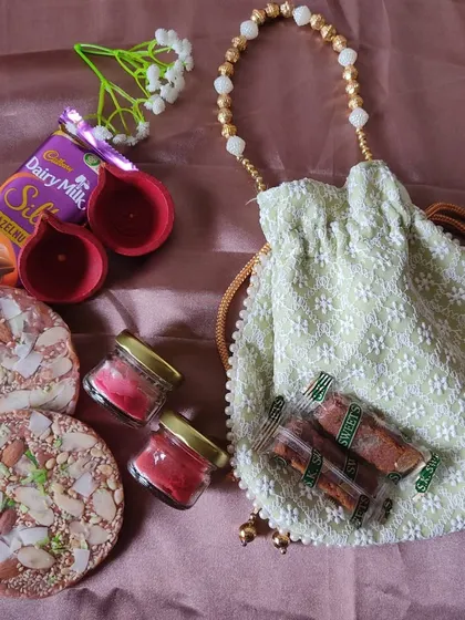 Celebrate the festival of lights with a traditional yet modern Diwali gift set. This hamper includes a beautiful potli bag, hand-painted diyas, scented candles, dry fruit chikki, and Dairy Milk Silk for a sweet touch.