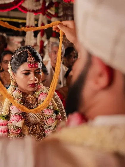 A key moment in a South Indian wedding ceremony, captured from an intimate over-the-shoulder perspective.