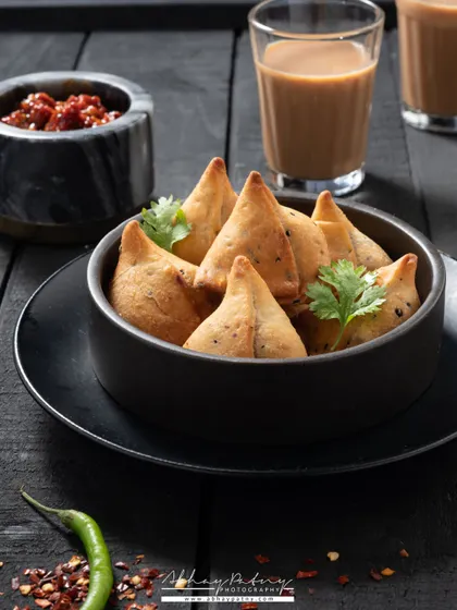 This shot of mini samosas with chai creates the perfect evening snack scene. The dark, moody lighting gives it a cozy and inviting atmosphere.