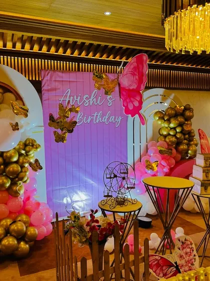 A whimsical butterfly-themed birthday for 'Avishi'. This setup combines gold and pink balloons, large butterfly cutouts, and a personalized backdrop for a sweet and stylish party.