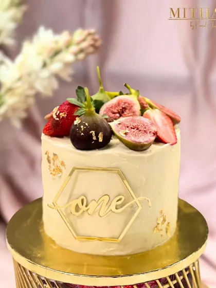 A delicate cake for a first birthday celebration. This vanilla bean cake is topped with fresh figs and strawberries, with a gold-dipped fig and a custom "one" cake topper for an elegant touch.