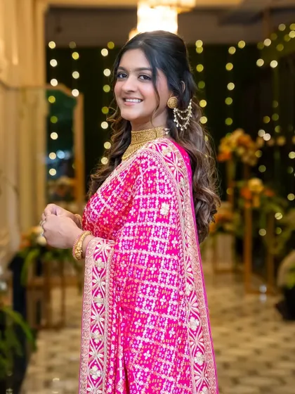 A beautiful, traditional look for a Lagan Lakhvanu ceremony. The bride's bright pink bandhani saree is paired with classic gold jewelry and a soft, glowing makeup look.